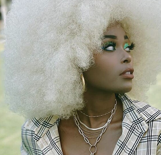 Perruque blanche aux cheveux afro type disco pour femme sur femme noire maquillée à bijoux.