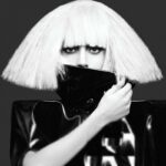 Photo en noir et blanc avec Lady Gaga qui cache la moitié de son visage en portant une perruque à frange blanche.