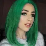 On voit une jeune femme maquillée qui arbore une perruque vert foncé.
