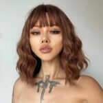 Femme avec un tatouage sur le cou avec une perruque châtain avec des cheveux ondulés et une frange