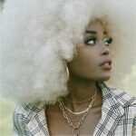 Perruque blanche aux cheveux afro type disco pour femme sur femme noire maquillée à bijoux.