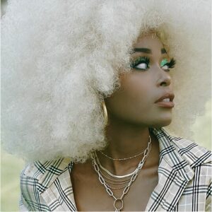 Perruque blanche aux cheveux afro type disco pour femme sur femme noire maquillée à bijoux.
