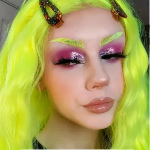 On voit la tête d'une jeune fille qui porte une perruque vert fluo et qui est très maquillée pour aller à une soirée.