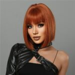buste de femme sur fond gris avec haut en simili cuir noir brillant couvrant une épaule portant une perruque rousse carré court avec cheveux lisses et frange