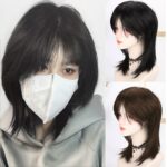 Femme portant un masque et une perruque noire. À droite de l'image, on voit la perruque de profil sur un mannequin.